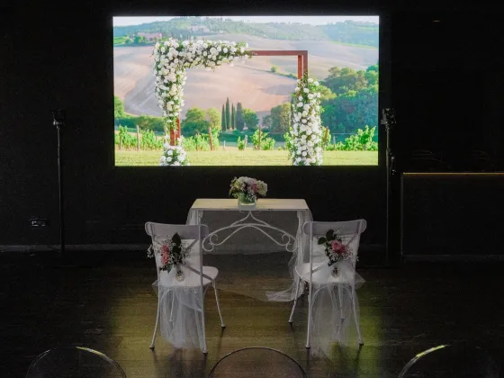 Allestimento per cerimonia matrimoniale nella Terrazza Colombo: due sedie decorate con tulle e fiori bianchi davanti a un tavolo nuziale, con sullo sfondo una grande proiezione di paesaggio naturale