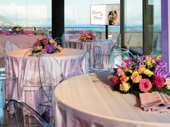 Sala allestita per ricevimento nella Terrazza Colombo: tavoli rotondi con tovaglie color lavanda, sedie trasparenti e centrotavola floreali con vista panoramica su Genova e il mare